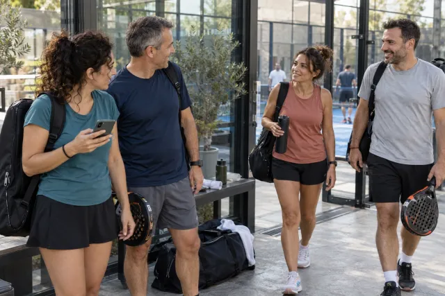 Four players meet at a padel club entrance, with one player holding a phone.